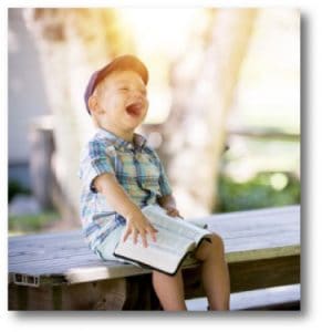 Lachender Junge mit Buch auf einer Bank sitzend