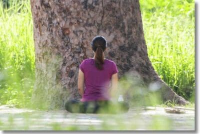 Frau sitzt meditierend vor einem grossem Baum
